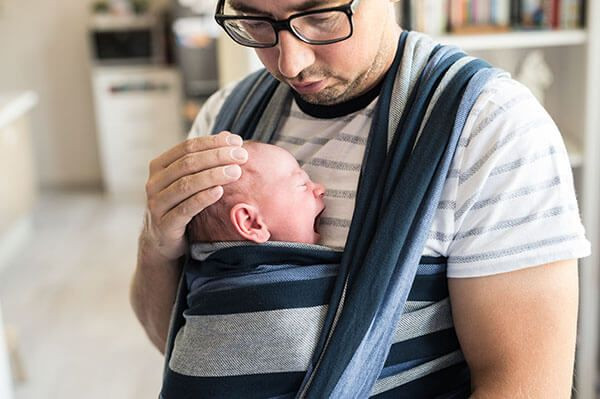 homem segurando um bebê com um sling.