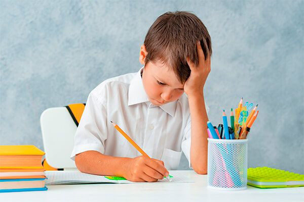 garoto com dificuldade de aprendizagem sentado com um caderno aberto e lápis nas mãos.