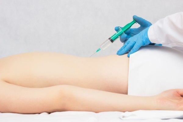 Mulher de bruços em maca, aplicação intramuscular de ozônio.